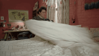 A Woman Is Making A Bed With A Map Of The World Hanging On The Wall Behind Her GIF