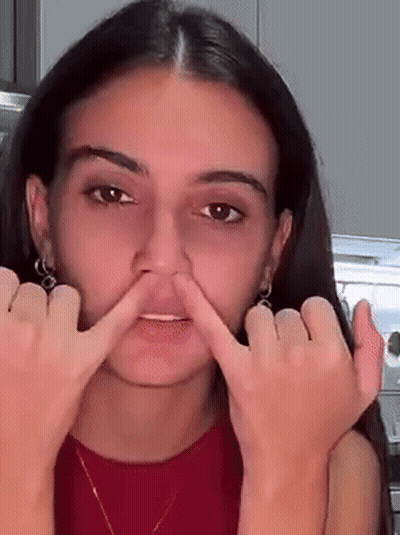 A Woman Is Making A Face With Her Fingers In Her Nose GIF