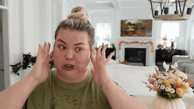 A Woman Is Making A Funny Face In A Living Room While Covering Her Ears With Her Hands . GIF