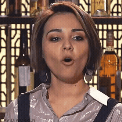 A Woman Is Making A Funny Face In Front Of A Bar With Bottles Of Alcohol In The Background . GIF
