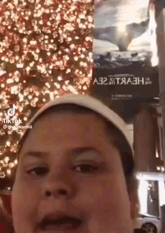 A Woman Is Making A Funny Face In Front Of A Christmas Tree And A Sign That Says A32 GIF