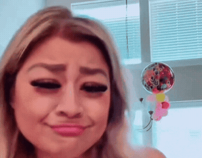 A Woman Is Making A Funny Face In Front Of A Window With Balloons Hanging From It . GIF