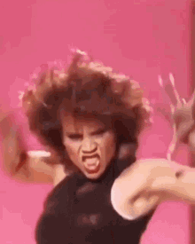 A Woman Is Making A Funny Face While Dancing In Front Of A Pink Wall . GIF