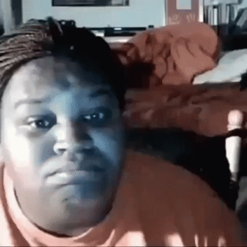 A Woman Is Making A Funny Face While Sitting In Front Of A Bed In A Bedroom . GIF