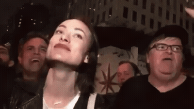 A Woman Is Making A Funny Face While Standing In Front Of A Crowd Of People . GIF