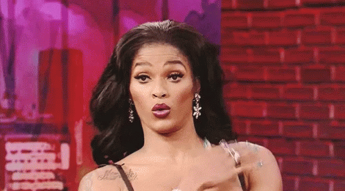A Woman Is Making A Funny Face While Standing In Front Of A Red Brick Wall . GIF