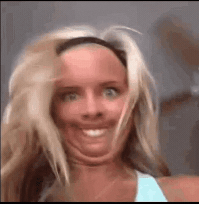 A Woman Is Making A Funny Face With Her Mouth Open And Her Hair Blowing In The Wind . GIF