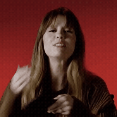 A Woman Is Making A Gesture With Her Hands In Front Of A Red Background While Wearing A Black Sweater . GIF