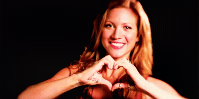 A Woman Is Making A Heart Shape With Her Hands In Front Of Her Face . GIF