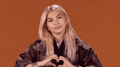 A Woman Is Making A Heart Shape With Her Hands On An Orange Background . GIF