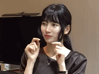 A Woman Is Making A Heart Shape With Her Hands While Sitting In Front Of A Computer Monitor . GIF