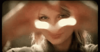 A Woman Is Making A Heart With Her Hands In Front Of Her Face . GIF
