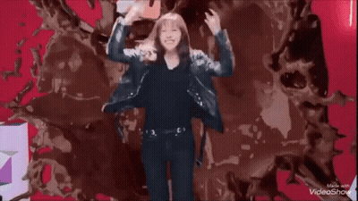 A Woman Is Making A Rock Sign With Her Hands While Dancing In Front Of A Colorful Background . GIF