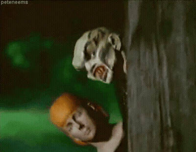 A Woman Is Peeking Out From Behind A Tree While A Zombie Is Looking At Her . GIF
