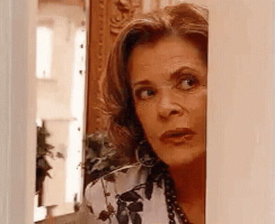 A Woman Is Peeking Out From Behind A Wall And Looking At The Camera . GIF