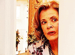 A Woman Is Peeking Out Of A Doorway And Making A Surprised Face . GIF