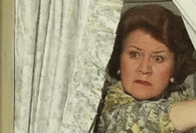 A Woman Is Peeking Out Of A Window With A Shocked Look On Her Face . GIF