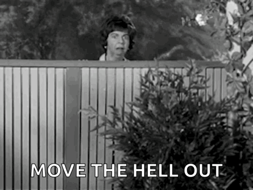 A Woman Is Peeking Over A Wooden Fence With The Words `` Move The Hell Out '' . GIF