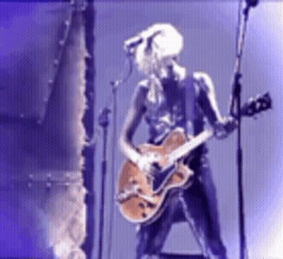 A Woman Is Playing A Guitar And Singing Into A Microphone GIF