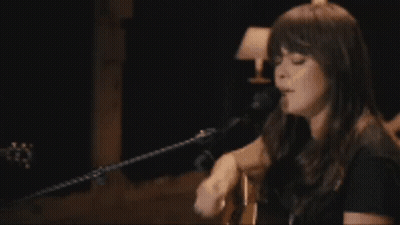 A Woman Is Playing A Guitar And Singing Into A Microphone GIF
