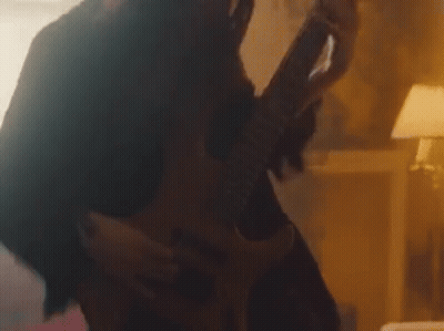 A Woman Is Playing A Guitar In A Dark Room While A Man Is Holding Her . GIF