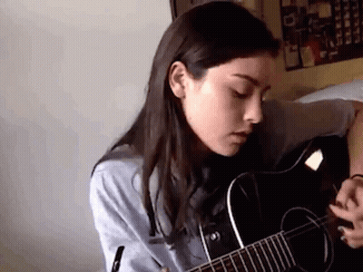 A Woman Is Playing A Guitar In A Room . GIF