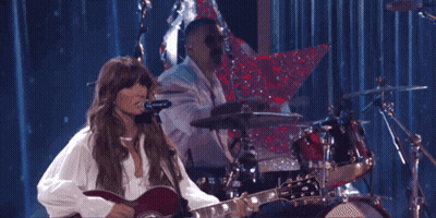 A Woman Is Playing A Guitar While A Man Plays Drums GIF