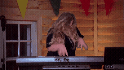 A Woman Is Playing A Keyboard In Front Of A Log Wall GIF