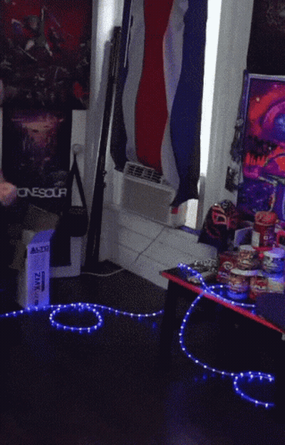 A Woman Is Playing A Video Game In A Room With A Red White And Blue Flag On The Wall GIF