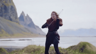 A Woman Is Playing A Violin In Front Of A Mountain And A Lake . GIF