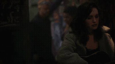 A Woman Is Playing An Acoustic Guitar In A Dark Room . GIF