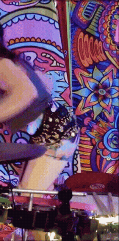 A Woman Is Playing Drums In Front Of A Colorful Wall Mural . GIF