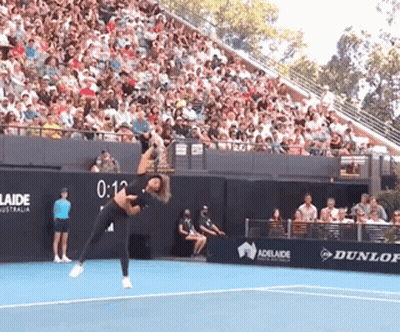 A Woman Is Playing Tennis In Front Of A Crowd And A Sign That Says Adelaide GIF