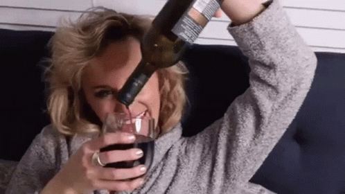 A Woman Is Pouring A Bottle Of Wine Into A Glass While Laying On A Couch . GIF