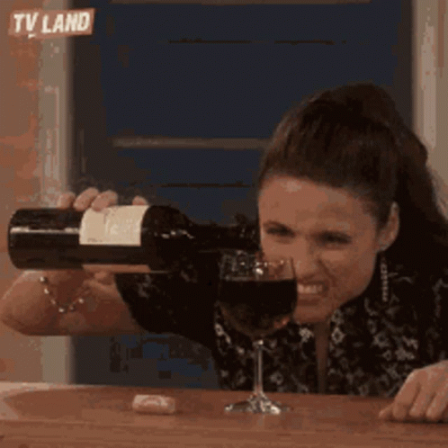 A Woman Is Pouring A Bottle Of Wine Into A Wine Glass . GIF