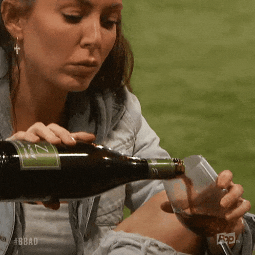 A Woman Is Pouring A Glass Of Wine From A Bottle With A Label That Says Z On It GIF