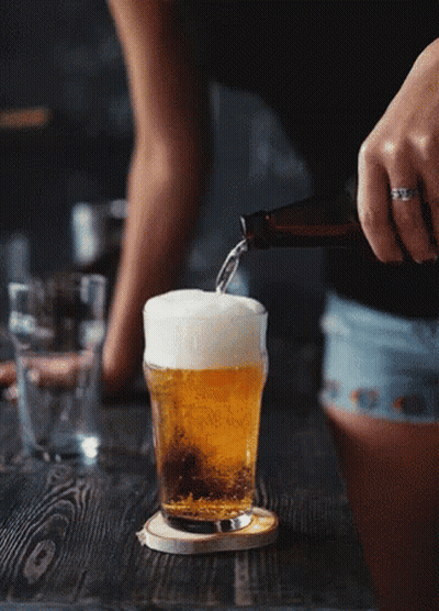 A Woman Is Pouring Beer Into A Glass On A Table GIF