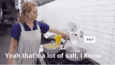 A Woman Is Pouring Salt Into A Pot Of Water . GIF