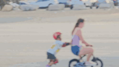 A Woman Is Pushing A Child On A Bicycle That Says ' Razor ' On It GIF