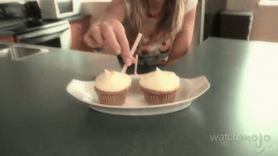 a woman is putting frosting on two cupcakes that are on a paper plate