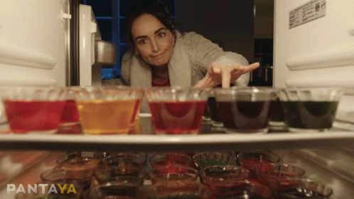 A Woman Is Reaching Into A Refrigerator Filled With Shot Glasses And Jelly GIF