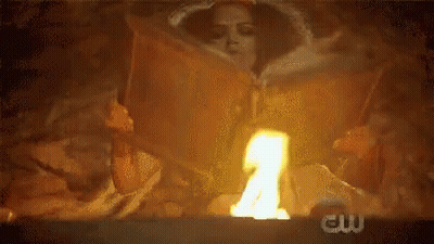 A Woman Is Reading A Book In Front Of A Fire With The Cw Logo In The Background . GIF