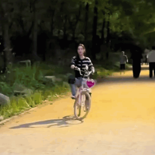 A Woman Is Riding A Bike Down A Dirt Path GIF