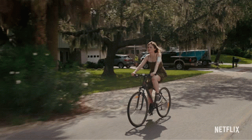 A Woman Is Riding A Bike Down A Street With A Netflix Logo On The Bottom GIF