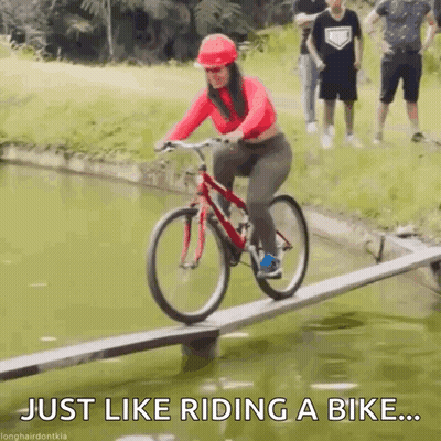 A Woman Is Riding A Bike On A Wooden Bridge Over A Body Of Water . GIF