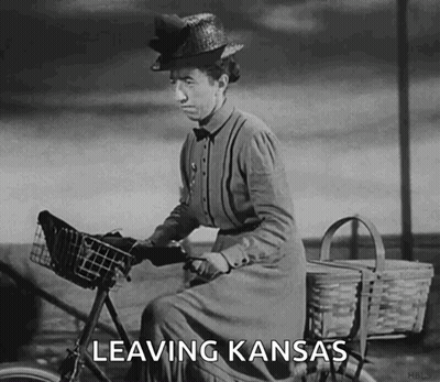 A Woman Is Riding A Bike With The Words Leaving Kansas Written On It GIF