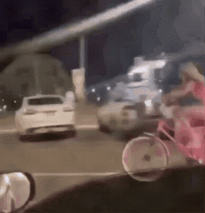 A Woman Is Riding A Pink Bicycle Down A Street Next To A Car . GIF