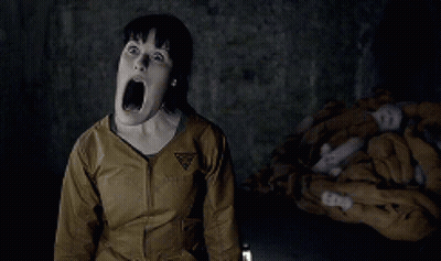 A Woman Is Screaming In A Dark Room With A Triangle Logo On Her Jacket GIF
