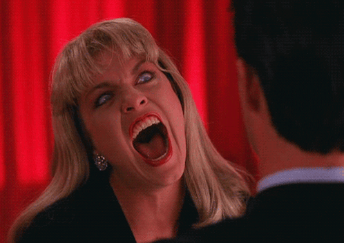A Woman Is Screaming In Front Of A Man With A Red Curtain Behind Her GIF