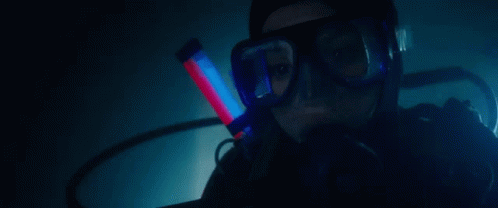 A Woman Is Scuba Diving In A Dark Room With A Red Light In Her Mouth . GIF